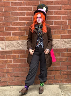 Trinity Coblentz dressed as the Mad Hatter standing in front of a brick wall